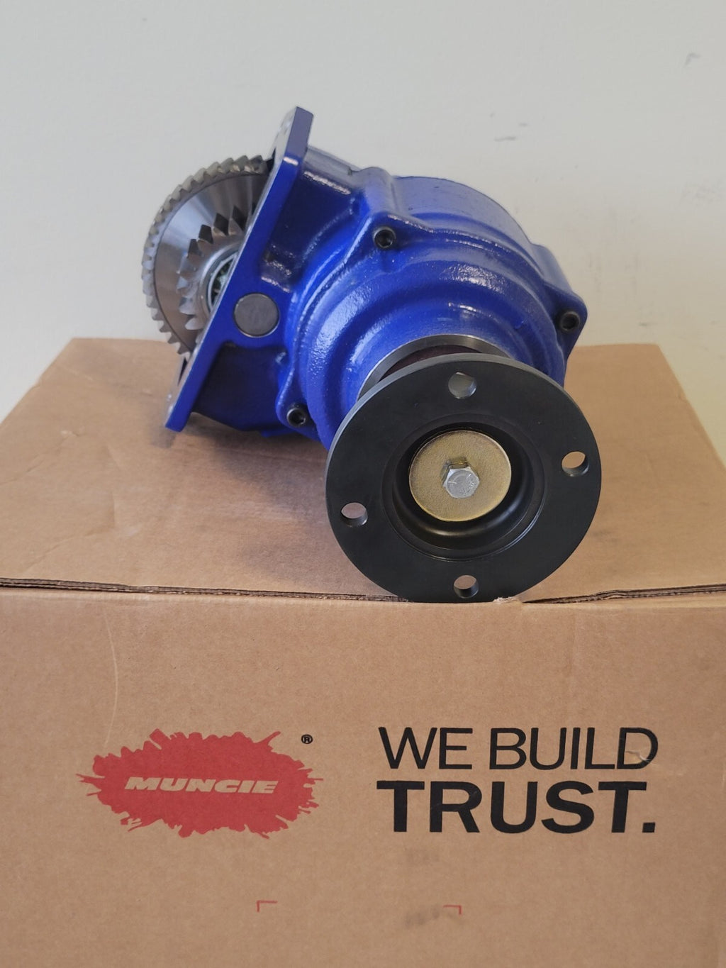 Mechanical component on a cardboard box with 'Muncie' branding and 'We Build Trust' slogan.